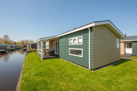 Moderne lodge kaldet Fuut 4 i Giethoorn, Holland, med grøn græsplæne og udsigt til en kanal under blå himmel.