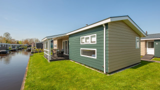 Moderne lodge kaldet Fuut 4 i Giethoorn, Holland, med grøn græsplæne og udsigt til en kanal under blå himmel.