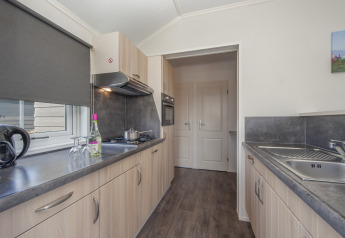 Modern kitchen at Stern 6 lodge in Giethoorn, Netherlands, with wood cabinets, stove, sink, and window blind.