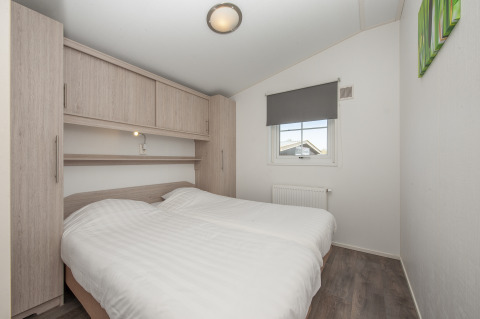 Schlafzimmer in der Lodge Stern 6 in Giethoorn, Niederlande, mit Doppelbett, Holzschränken und Fenster.