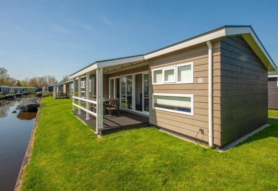 Modernes Ferienhaus am Wasser in Giethoorn, Niederlande, mit Terrasse, Rasen und Boot am Kanal.