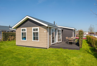 Außenansicht der Lodge Stern 6 in Giethoorn, Niederlande, mit Terrasse und grüner Rasenfläche bei Sonne.