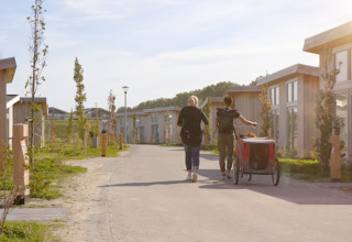 Dos personas caminan por Water Village, un parque vacacional en Zelanda, Países Bajos, entre cabañas modernas.