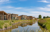 Feriehytter ved vandet på Water Village feriepark i Zeeland, Holland, solrig dag med grønt og blå himmel.