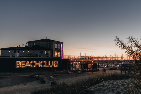 Solnedgang ved Water Village, Zeeland, med strandklub, cykel og lystbådehavn i baggrunden.