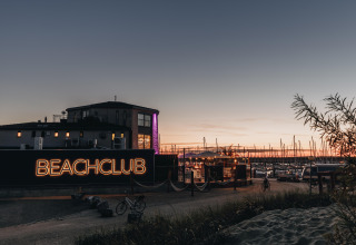 Avondlicht bij Water Village, Zeeland, met verlichte Beachclub, fietsen en een jachthaven op de achtergrond.