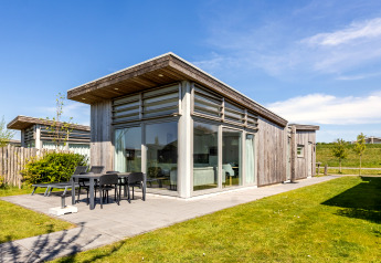 Lodge 4 moderne avec façade en bois, grandes baies vitrées et terrasse aménagée par une journée ensoleillée.
