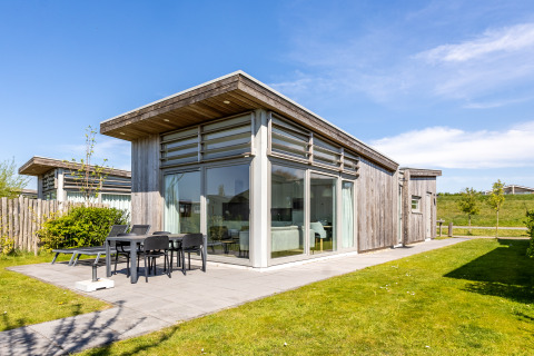 Moderna Lodge 4 con fachada de madera, grandes ventanales y terraza con muebles de jardín en un día soleado.