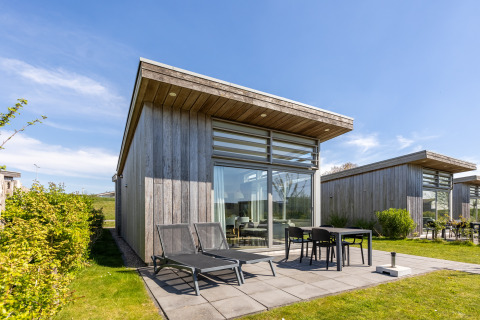 Moderne Lodge mit großen Fenstern und Terrasse, Sonnenliegen am Water Village in den Niederlanden.
