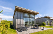 Moderne Lodge mit großen Fenstern und Terrasse, Sonnenliegen am Water Village in den Niederlanden.