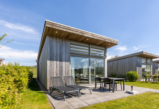 Moderne Lodge mit großen Fenstern und Terrasse, Sonnenliegen am Water Village in den Niederlanden.