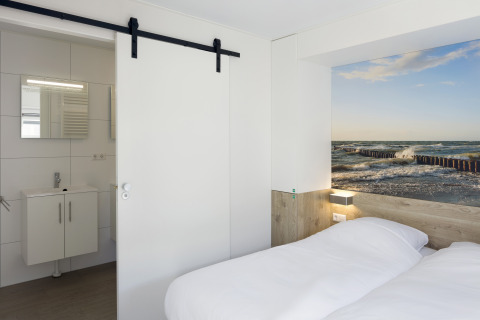 Schlafzimmer in Lodge 4 im Water Village, Niederlande, mit Doppelbett, Bad und Meeresbild an der Wand.