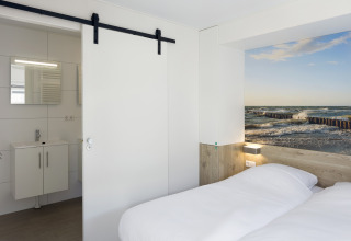 Schlafzimmer in Lodge 4 im Water Village, Niederlande, mit Doppelbett, Bad und Meeresbild an der Wand.