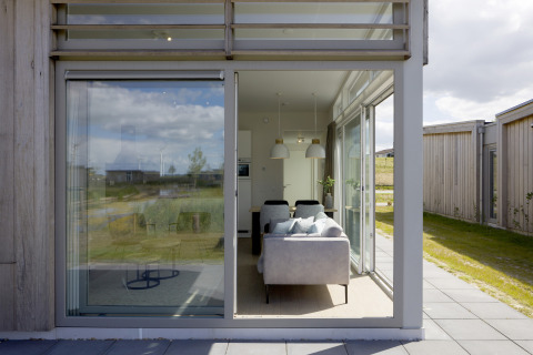 Zicht door grote ramen op een moderne woonkamer in Lodge 4, Water Village, Nederland, met natuur buiten.