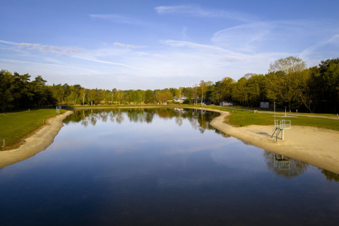 Foto van een rustig meer met zandstrand en groene bomen in Bospark 't Wolfsven, Noord-Brabant, Nederland.