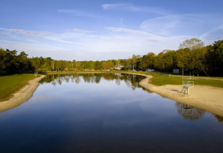 Billede af en fredelig sø med sandstrand og grønne træer i Bospark 't Wolfsven, Nord-Brabant, Nederlandene.