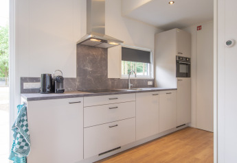 Moderne lille køkken i Timber Cottage 4 på Bospark 't Wolfsven med hvide skabe og trælaminatgulv.