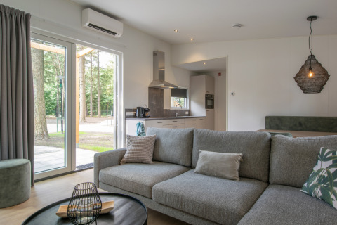 Living room and kitchen in Timber Cottage 4 at Bospark 't Wolfsven, Netherlands, with forest view outside.