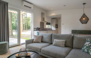 Moderne stue og køkken i Timber Cottage 4 på Bospark 't Wolfsven, med stor sofa og udsigt til natur.