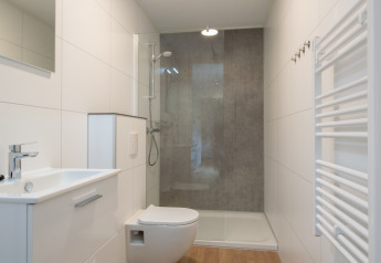 Moderne lille badeværelse med bruser, væghængt toilet, håndvask og hvidt vægpanel i Timber Cottage 4.