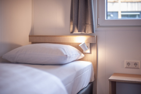 Letto moderno con lenzuola bianche, abat-jour e finestra in Timber Cottage 4 presso Bospark 't Wolfsven, Paesi Bassi.