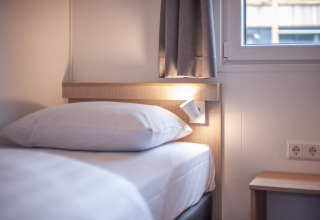Letto moderno con lenzuola bianche, abat-jour e finestra in Timber Cottage 4 presso Bospark 't Wolfsven, Paesi Bassi.