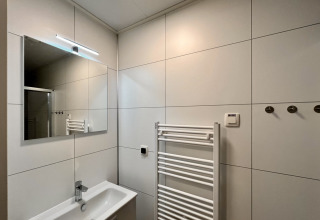 Moderne badeværelse i Timber Cottage 6 med spejl, vask og håndklædetørrer i Bospark 't Wolfsven, Holland.