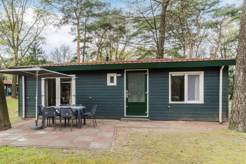 Chalet WVR6 at Bospark 't Wolfsven featuring a patio, outdoor dining set, and umbrella in wooded area.