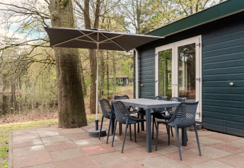 Buiten eethoek met parasol aan een chalet in Bospark 't Wolfsven, Nederland, tussen de bomen.