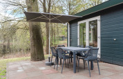 Área de comedor exterior con sombrilla en el chalet WVR6 de Bospark 't Wolfsven, Países Bajos, entre árboles.