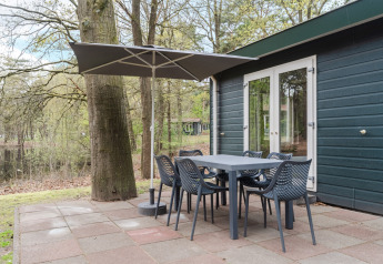 Terrasse mit Tisch, Stühlen und Sonnenschirm an einem Chalet im Bospark 't Wolfsven, Niederlande.