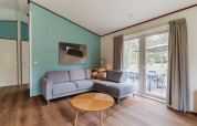 Living room in chalet WVR6 at Bospark 't Wolfsven with grey corner sofa, wood table, and patio view.