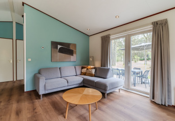 Sala de estar en el chalet WVR6 en Bospark 't Wolfsven con sofá gris, mesa de madera y vista a la terraza.