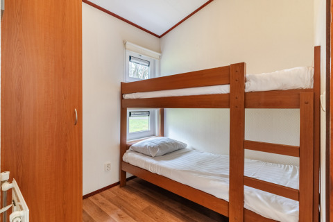 Dormitorio pequeño del chalet WVR6 en Bospark 't Wolfsven, Países Bajos, con litera y suelo de madera.