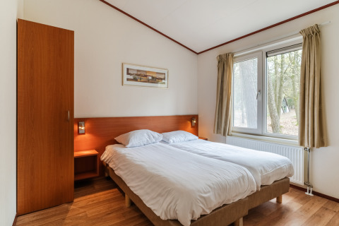 Dormitorio del chalet WVR6 en Bospark 't Wolfsven, Países Bajos, con cama doble y gran ventana.
