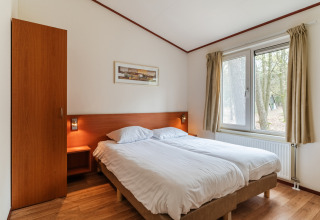 Bedroom in chalet WVR6 at Bospark 't Wolfsven, Netherlands, featuring a double bed and forest view.