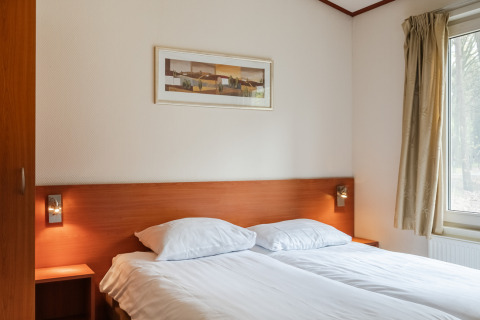 Soveværelse i chalet WVR6 på Bospark 't Wolfsven i Holland med dobbeltseng, natborde og vindue.