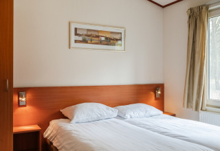 Chambre dans le chalet WVR6 au Bospark 't Wolfsven, Pays-Bas, avec lit double et table de chevet.