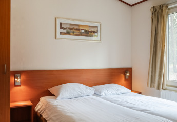 Soveværelse i chalet WVR6 på Bospark 't Wolfsven i Holland med dobbeltseng, natborde og vindue.