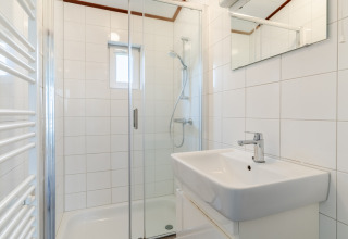 Moderne badeværelse med bruseniche, hvid håndvask og spejl i chalet WVR6, Bospark 't Wolfsven.