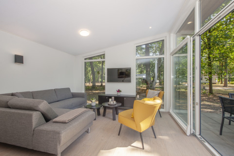 Bright living room in Lodge 6 tiny house at Bospark 't Wolfsven, Netherlands, with sofa and large windows.