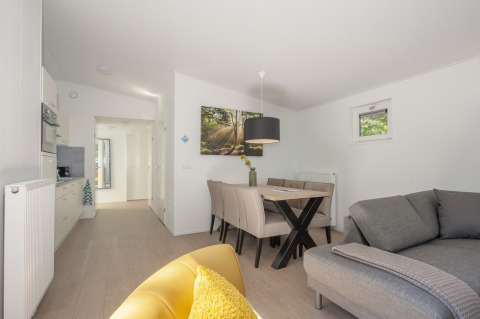 Interno luminoso e moderno di una tiny house presso Lodge 6, Bospark 't Wolfsven, con divano, tavolo e cucina.
