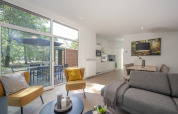 Lys og moderne stue i Lodge 6 på Bospark 't Wolfsven med store vinduer, udsigt til skov og udendørs terrasse.