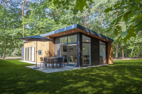 Modern Lodge 4 tiny house in the woods with large windows, patio, sun umbrella and outdoor table set.