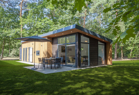 Modern Lodge 4 tiny house in the woods with large windows, patio, sun umbrella and outdoor table set.