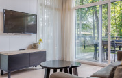 Sala de estar en Lodge 4 en Bospark 't Wolfsven, Países Bajos, con TV, mesa y vistas al jardín.