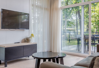 Soggiorno del Lodge 4 al Bospark 't Wolfsven, Paesi Bassi, con TV, tavolini e vista sul patio.