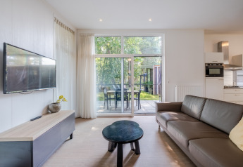 Lys stue i Lodge 4, Bospark 't Wolfsven, Nederlandene, med sofa, tv, terrasse og udsigt til haven.