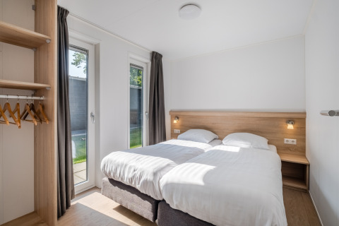 Modern tiny house bedroom with two single beds, wooden wardrobe, large windows and minimal decor.