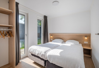 Camera moderna di tiny house con due letti singoli, armadio aperto e grandi finestre luminose.